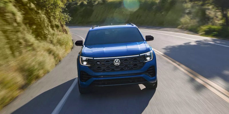 Blue SUV drives quickly on a winding road with green hillsides, motion blur showing speed.