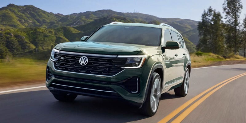 Dark green Volkswagen Atlas SUV driving on a winding road with green mountains in the background.