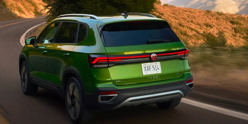 Bright green SUV, seen from the rear-right, driving on a winding road through sunlit hills.